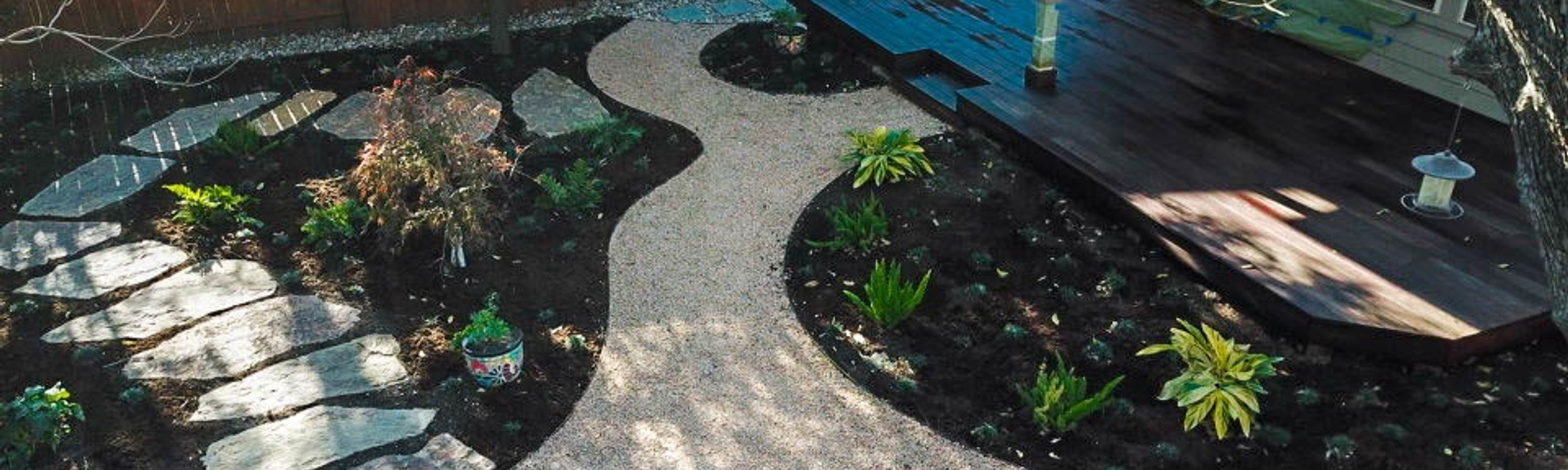 Wood deck with a flagstone pathway and planting beds in a shaded Riverplace garden
