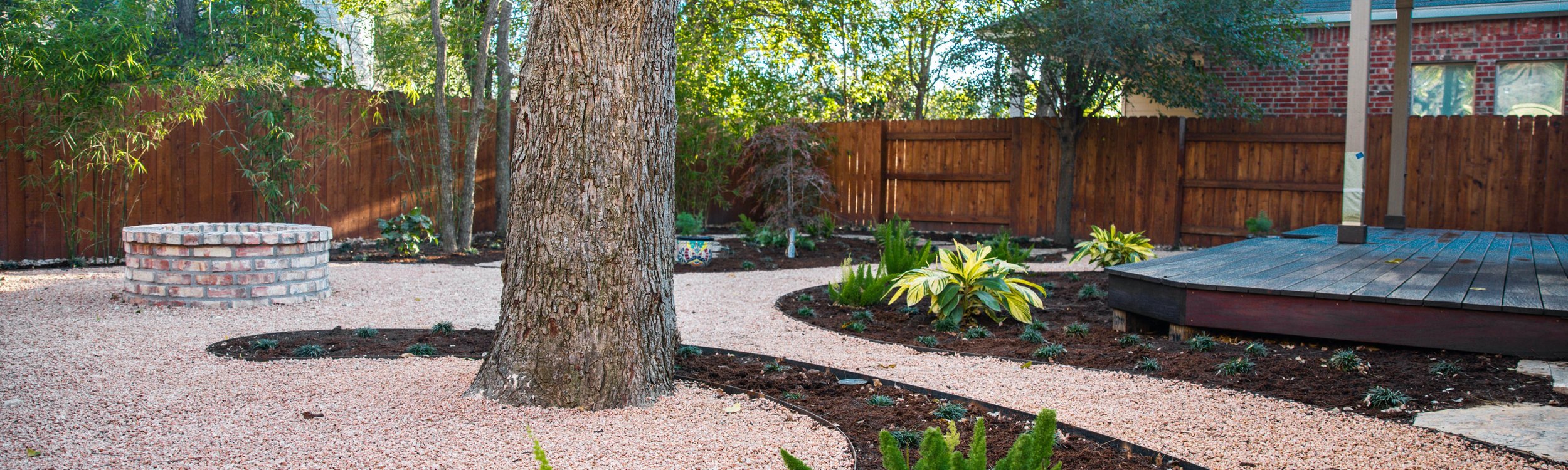 Fresh plantings filling decomposed granite beds around a deck and fire pit in a Riverplace, Austin landscape