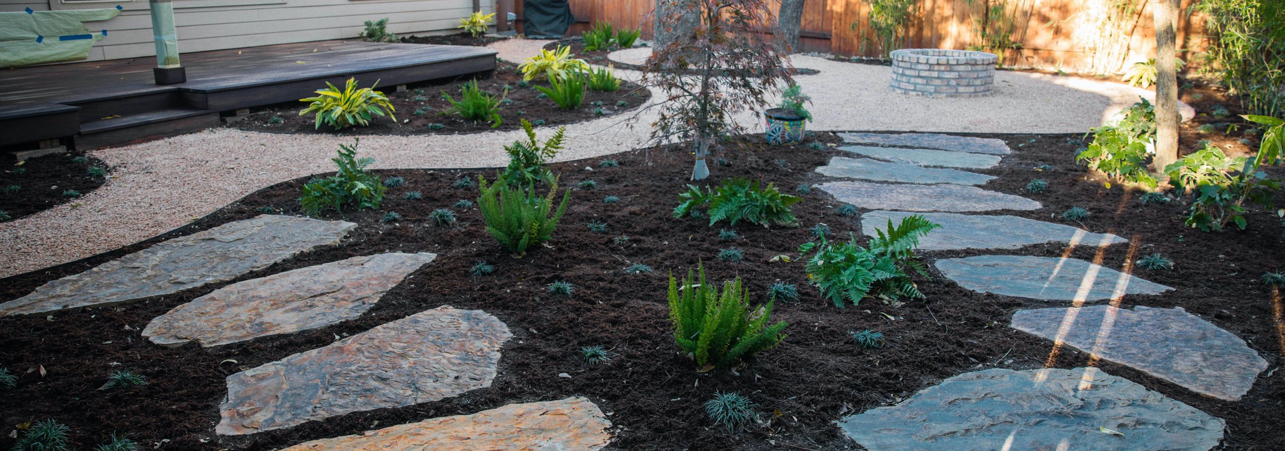 Wide view of the flagstone pathway, fire pit, and layered shade planting beds