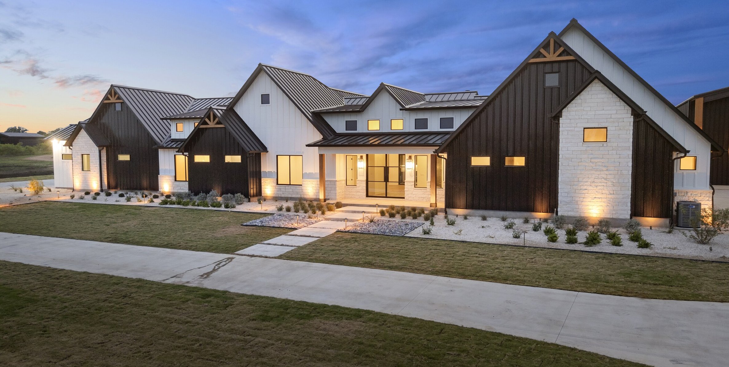 Aerial view at dusk of the finished front yard with gravel xeriscape beds, zoysia lawn, and landscape lighting