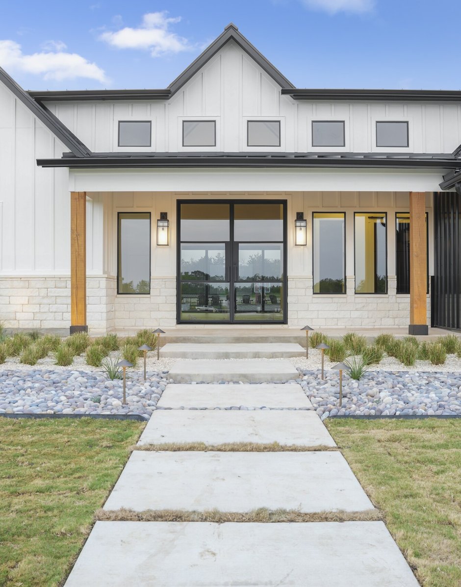 Concrete slab walkway framed by a river rock panel, steel edging, and bronze path lights at the front entry