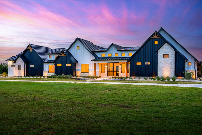 Modern farmhouse front yard at sunset with uplit cream limestone, low path lights, and native plantings in white gravel foundation beds set back from the slab on a new build in Rosanky, Texas