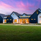 Modern farmhouse front yard at sunset with uplit cream limestone, low path lights, and native plantings in white gravel foundation beds set back from the slab on a new build in Rosanky, Texas