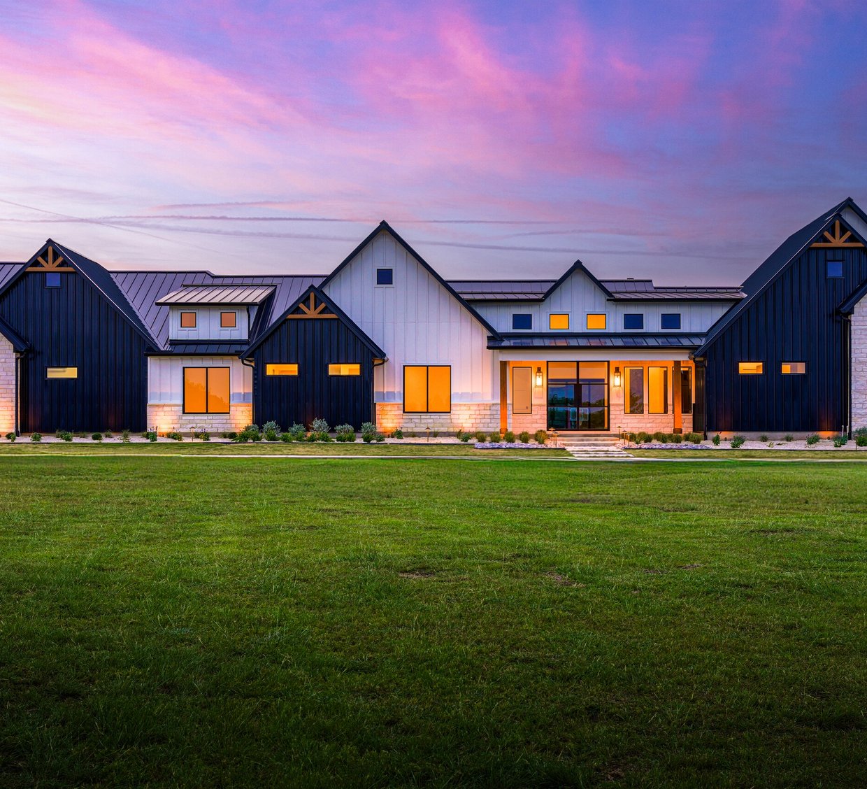 Rosanky new construction home with a native xeriscape, steel edged gravel beds, and a fresh zoysia lawn at sunset