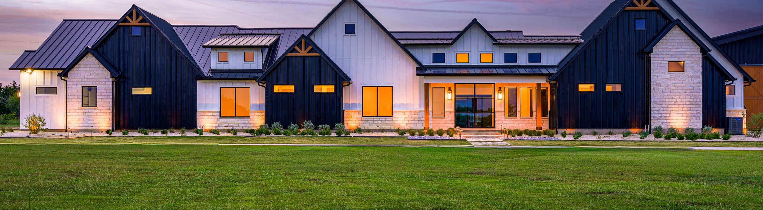 Modern farmhouse in Rosanky, TX at sunset with a new zoysia lawn and native xeriscape beds lit by low voltage landscape lighting