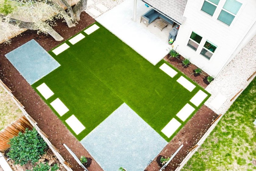 Aerial view of a Round Rock backyard with an artificial turf panel, stepping stones, gravel, and planting beds replacing a struggling lawn