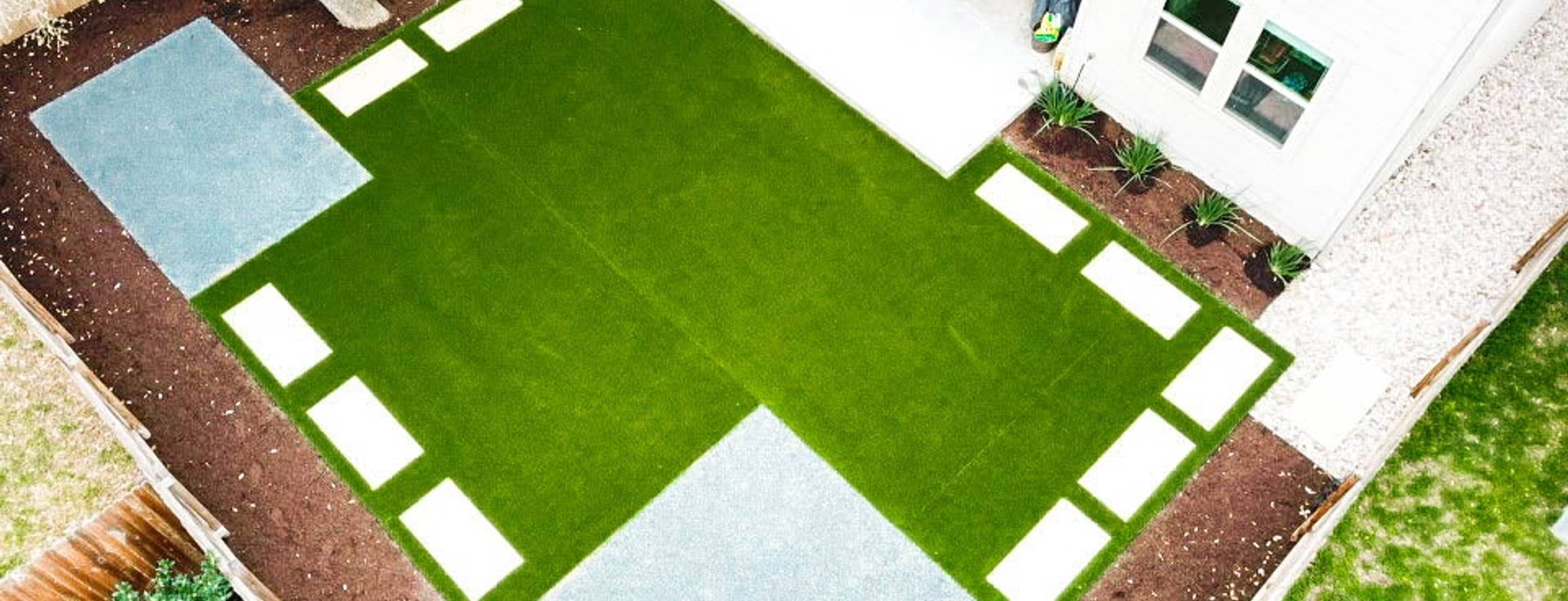Round Rock backyard with cream pavers set into synthetic turf in a checkerboard pattern, aerial view, by Thrive Landscape and Design