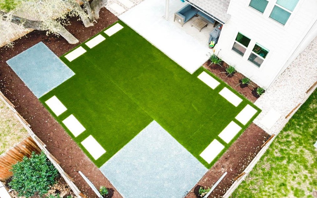 Aerial view of a Round Rock backyard with an artificial turf panel, stepping stones, gravel, and planting beds replacing a struggling lawn
