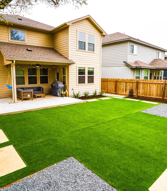 Healthy green turf, stepping stones, and planting beds in a Round Rock backyard