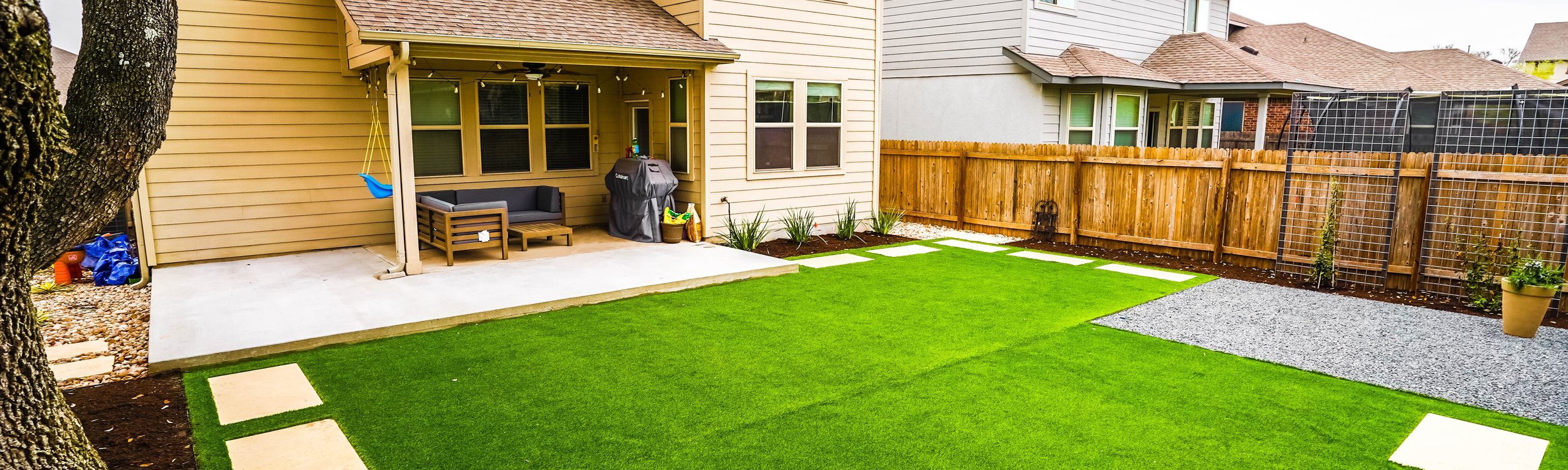 Artificial turf with stepping stones, a gravel patio, and planting beds in a Round Rock checkered garden