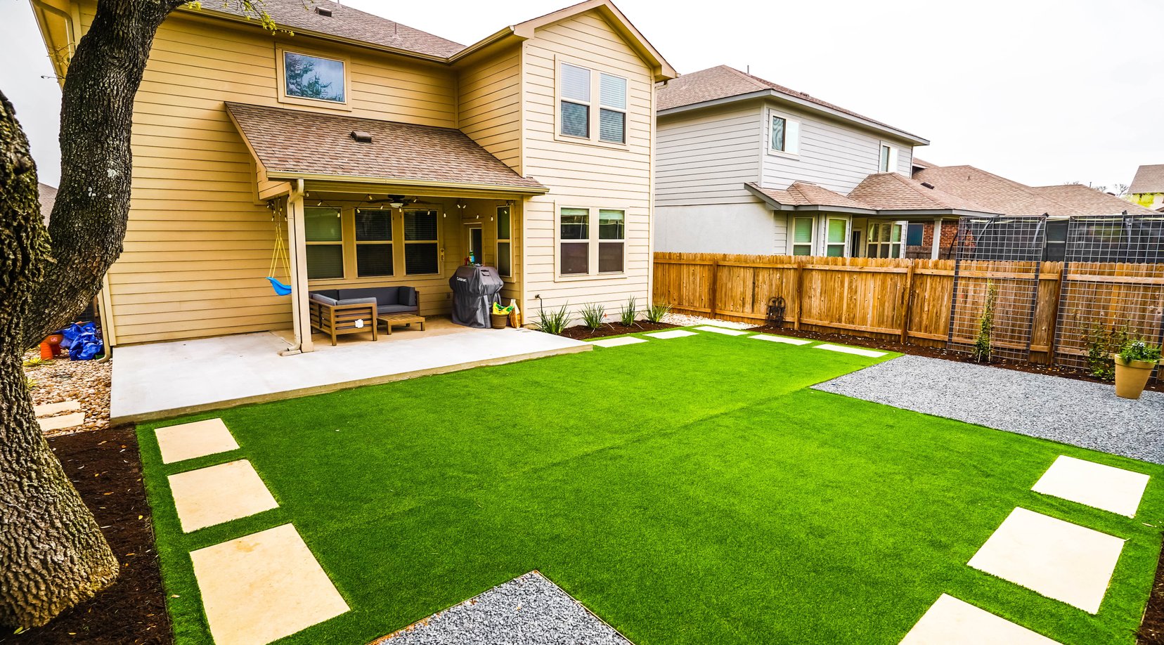 Cream pavers set into synthetic turf with decomposed granite zones and planting beds