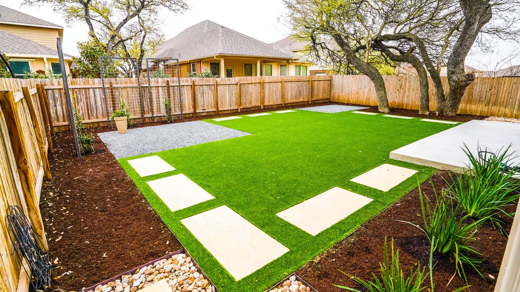 Fresh turf lawn set between stepping stones and river-rock beds at a Round Rock home