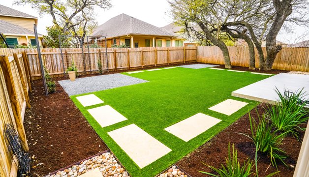 Artificial turf with stepping stones, gravel, and river rock in a Round Rock backyard