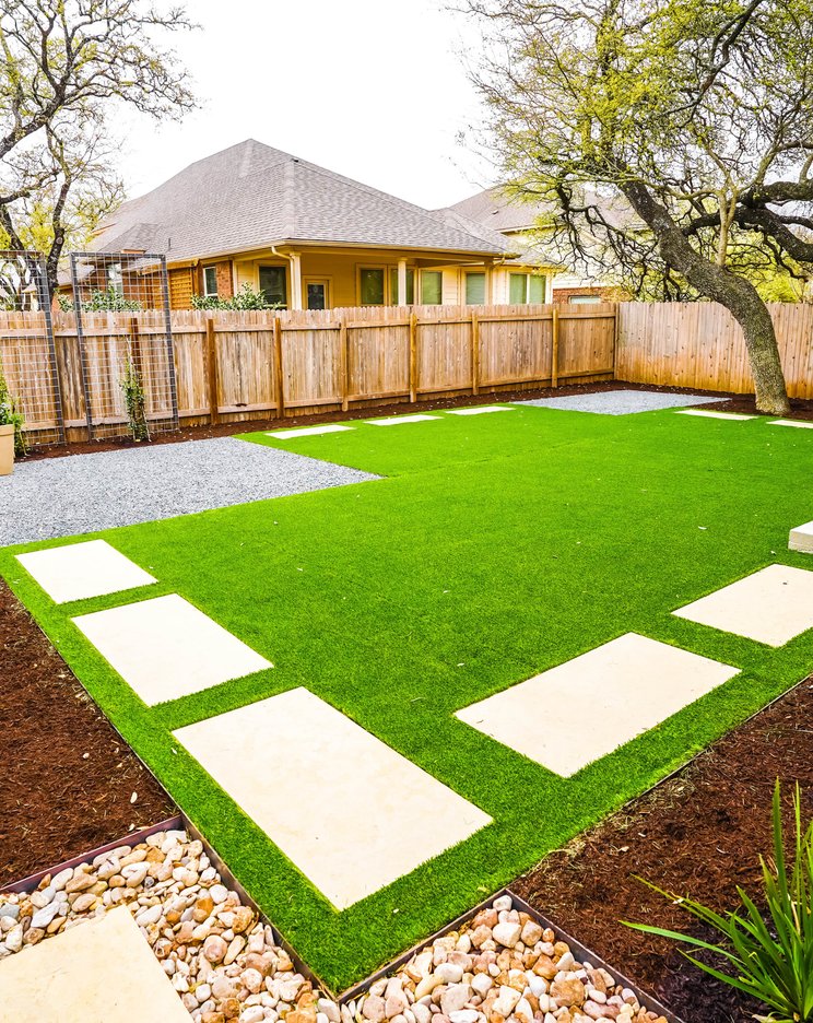 Artificial turf with stepping stones, gravel, and planting beds in a Round Rock yard