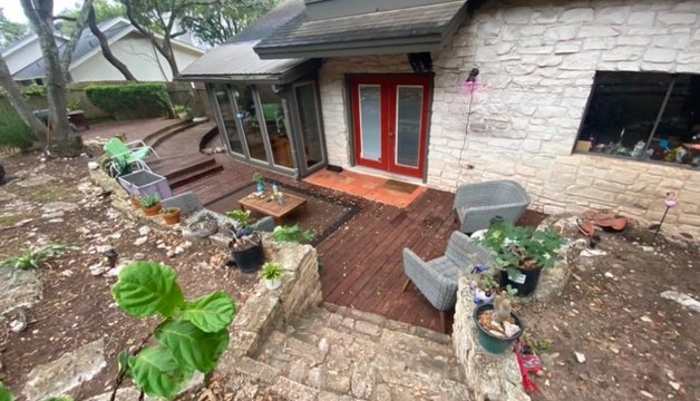 Tired sloped backyard before a landscape renovation, with an old wood deck in Austin