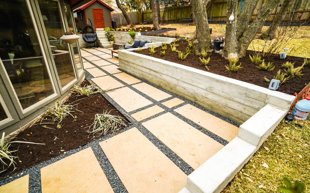 Terraced Austin backyard near Shoal Creek with a concrete retaining wall, gravel, a flagstone pathway, and planting beds that manage grade and drainage