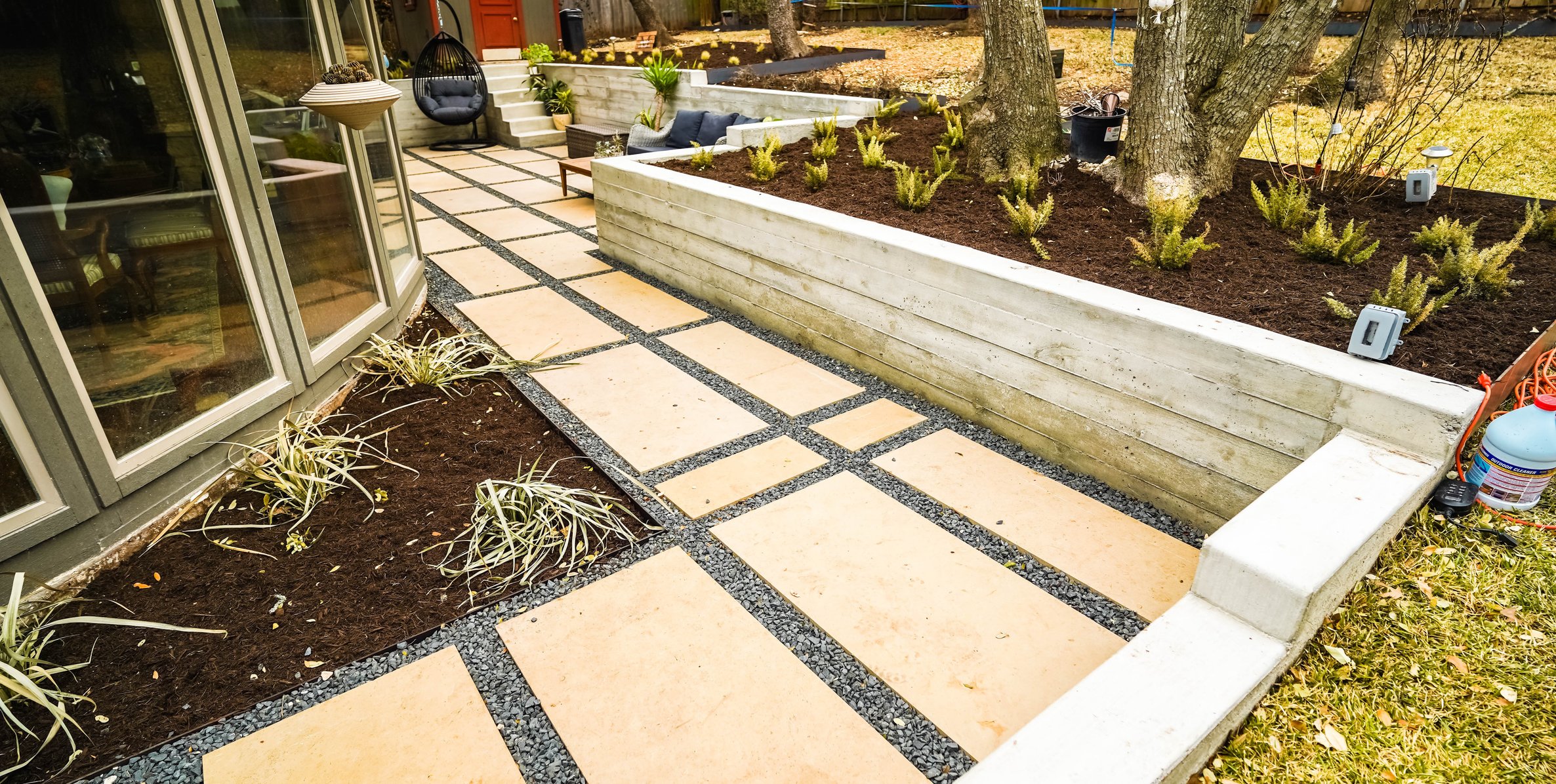 Flagstone pathway and gravel set against a board-formed concrete retaining wall with planting beds