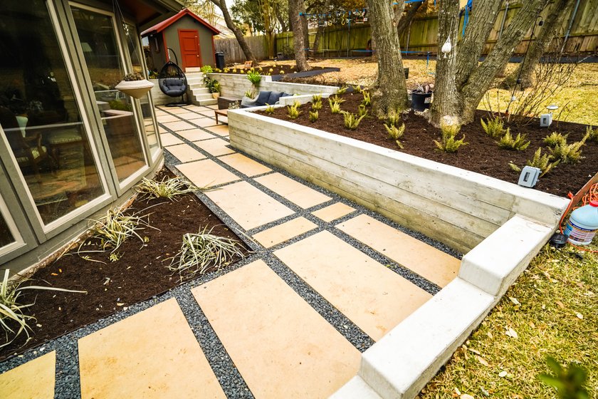 Terraced Austin backyard near Shoal Creek with a concrete retaining wall, gravel, a flagstone pathway, and planting beds that manage grade and drainage