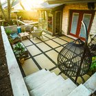 Cream large-format paver patio with black gravel joints, lounge seating, and hanging egg chairs below board-formed concrete retaining walls and concrete steps in a Shoal Creek backyard in central Austin