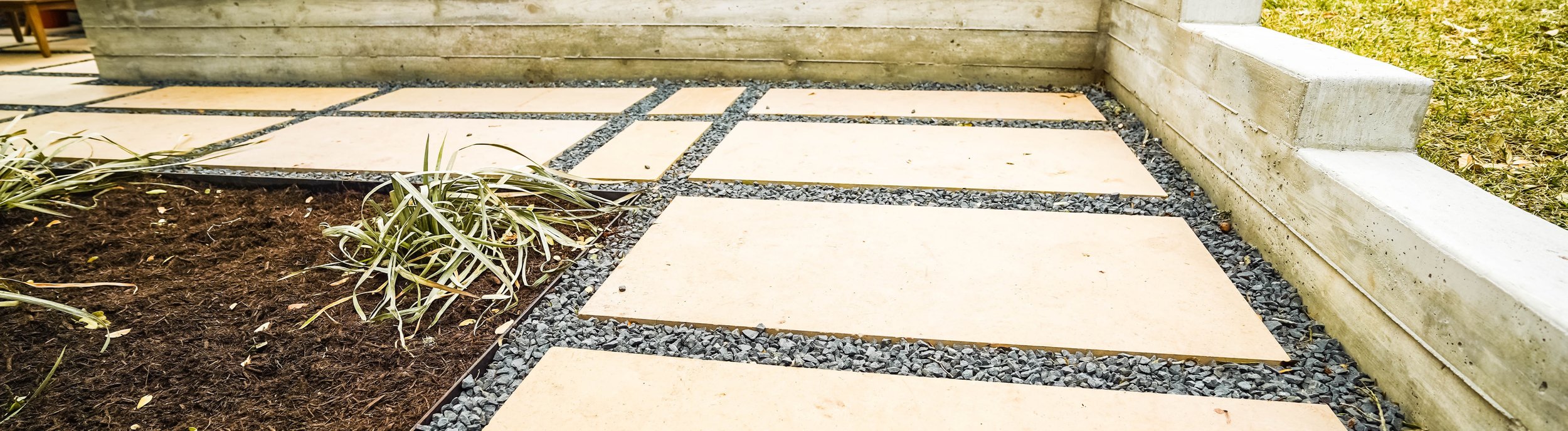 Board-formed concrete retaining wall with built-in steps holding back a raised lawn above a large-format paver and gravel patio in an Austin backyard near Shoal Creek