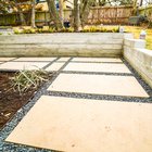 Board-formed concrete retaining wall with built-in steps holding back a raised lawn above a large-format paver and gravel patio in an Austin backyard near Shoal Creek