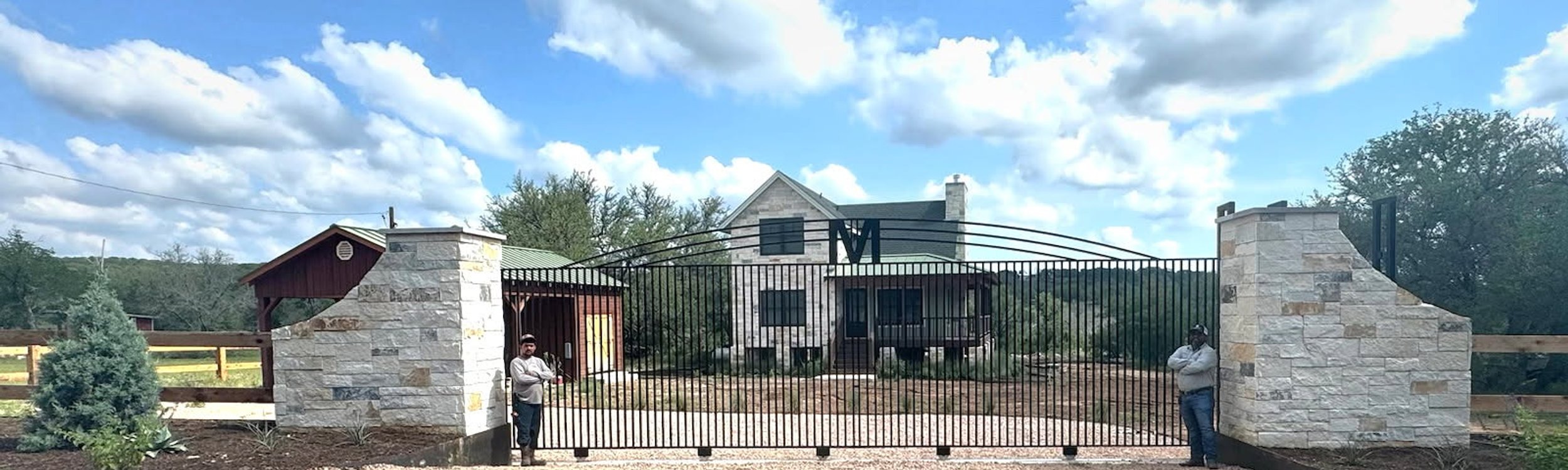 Wide iron driveway entry gate set between limestone columns at a Hill Country ranch home near Austin