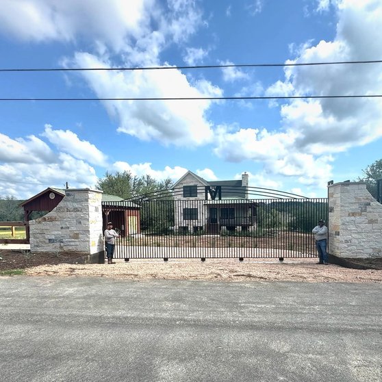 Custom ranch entry feature with stone columns and an iron gate at a Smithville home