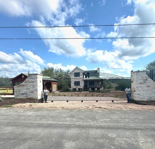 Driveway entry framed by stone columns and an iron gate at a Central Texas property
