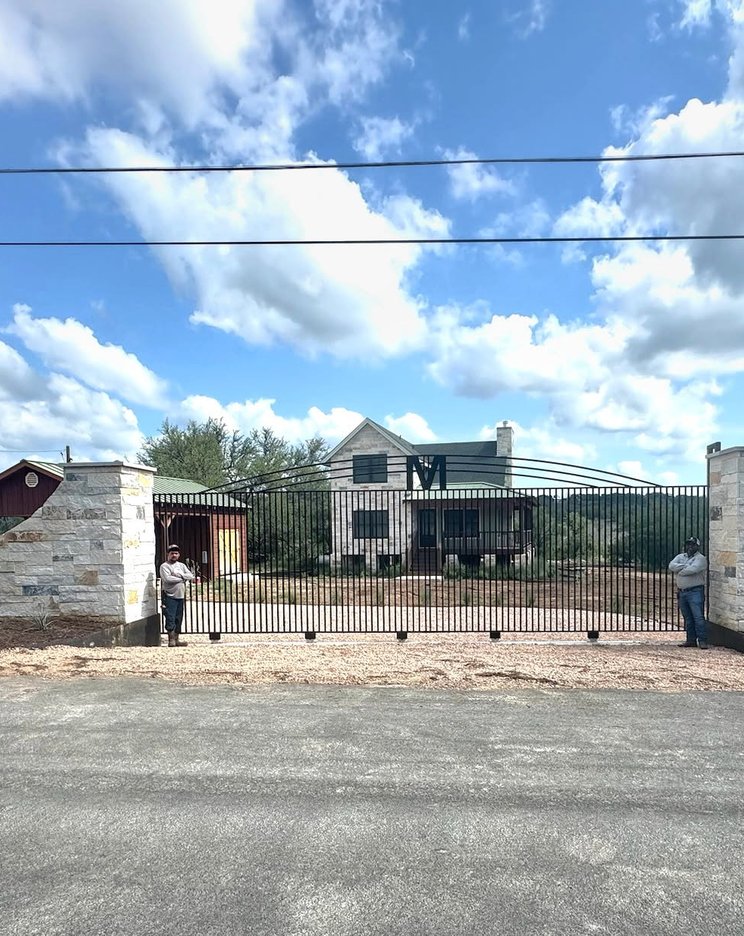 Wide iron driveway gate between limestone columns at a Hill Country ranch entry