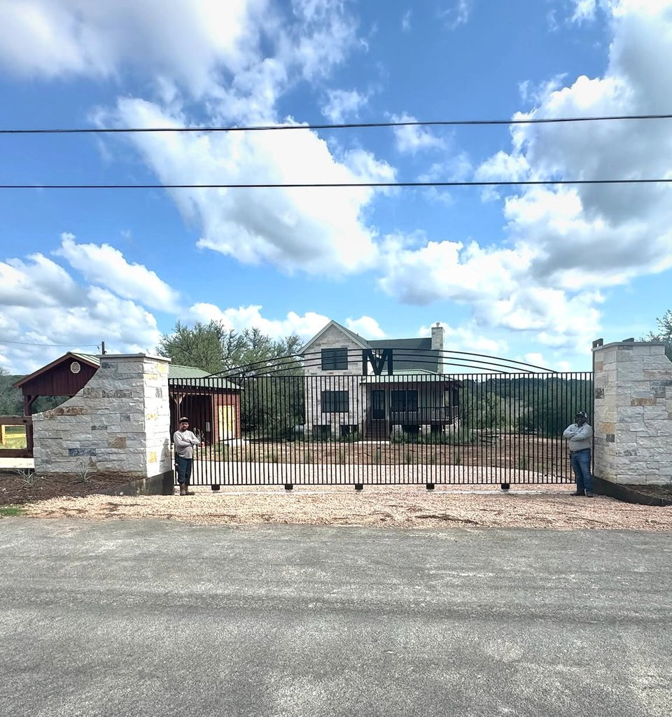 Smithville ranch entry with a wide iron driveway gate between limestone columns