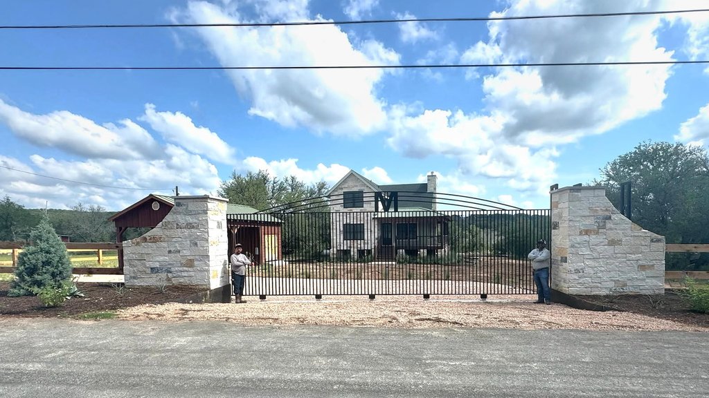 Designed iron driveway gate set between limestone columns at a ranch home entry