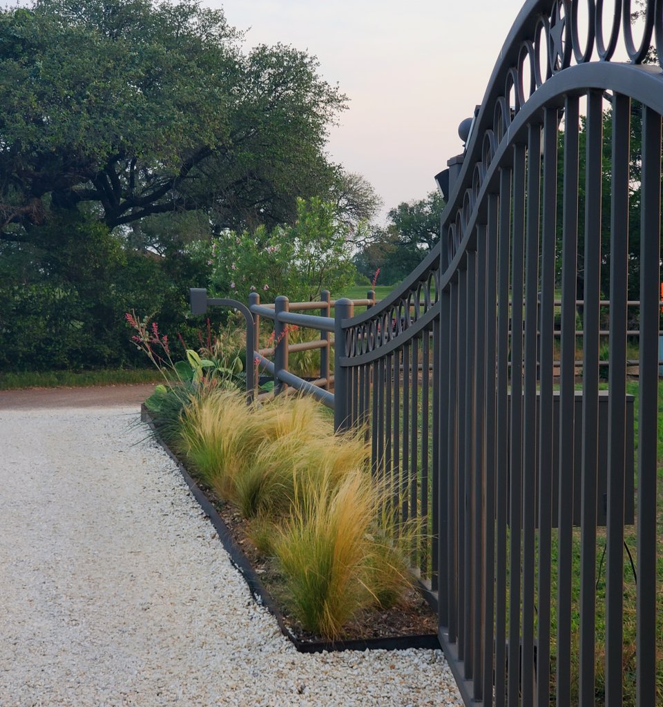 Ornamental iron fence and gate running along a gravel ranch driveway