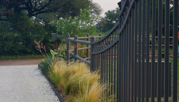 Ornamental iron fence and gate along a gravel driveway at a Smithville-area ranch