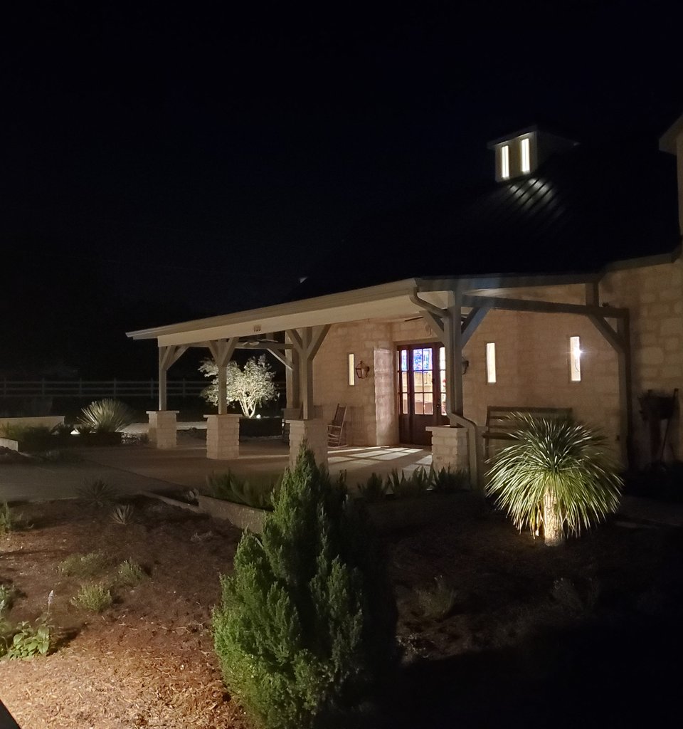 Smithville ranch with a custom timber-frame pavilion, metal roof, and stone columns lit at night