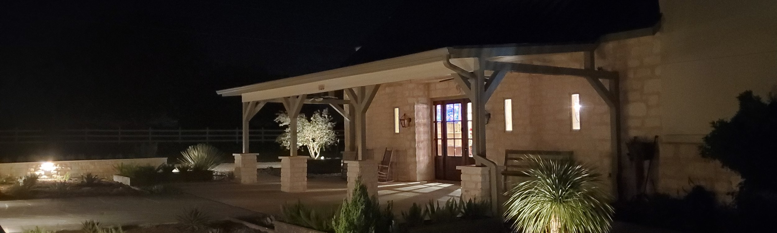 Custom timber-frame pavilion with a metal roof and stone columns lit at night at a Central Texas home