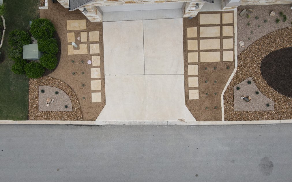 Aerial view of a Spicewood front yard where a concrete driveway is framed by cut limestone pavers set in decomposed granite, with river rock and gravel xeriscape beds on both sides