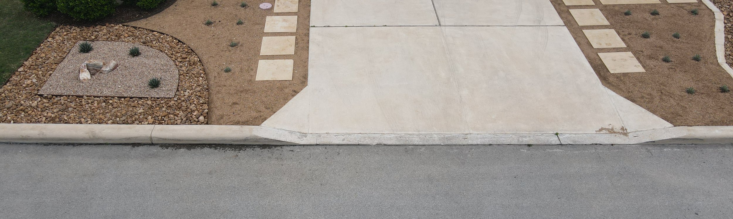 Front-of-home driveway with limestone pavers, gravel xeriscape beds, and a stone-clad garage in the Austin area