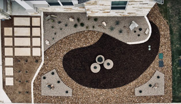 Aerial view of a front yard with limestone pavers set in gravel xeriscape beside a concrete driveway in the Austin area