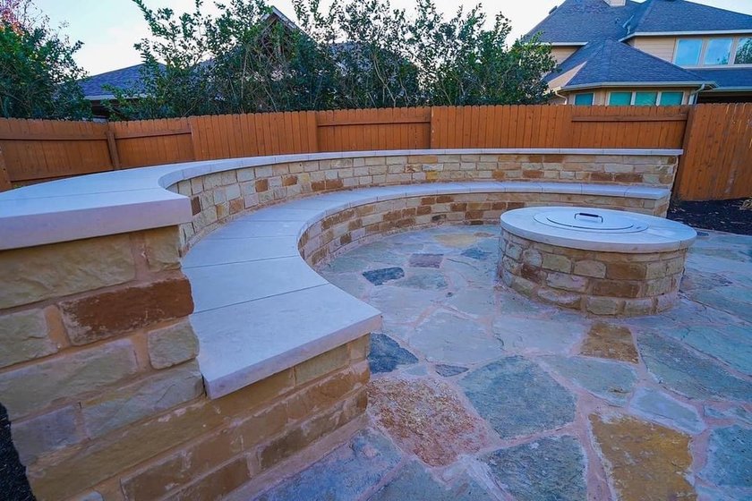 Built-in stone fire pit with a curved bench seating wall on a flagstone patio in a Steiner Ranch backyard near Austin