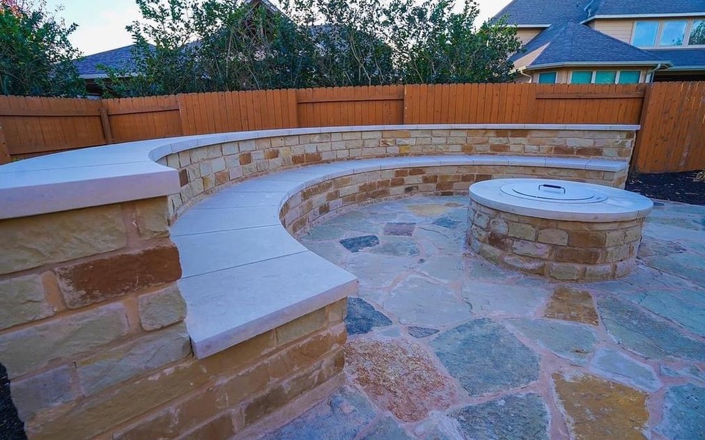 Built-in stone fire pit with a curved bench seating wall on a flagstone patio in a Steiner Ranch backyard near Austin