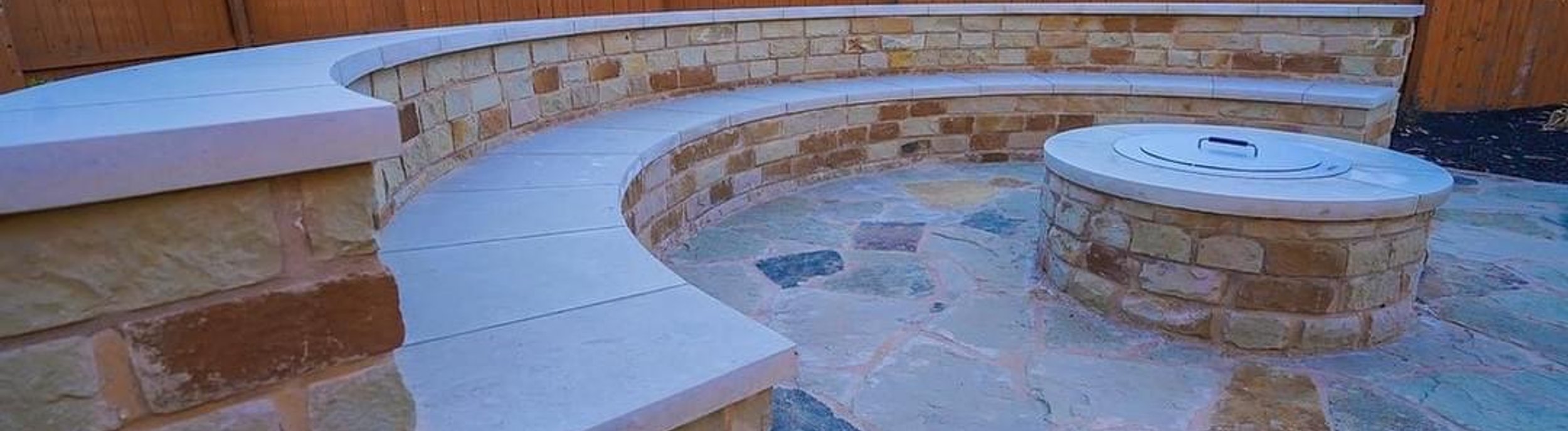 Built-in stone fire pit with a curved bench seating wall on a flagstone patio in a Steiner Ranch backyard near Austin