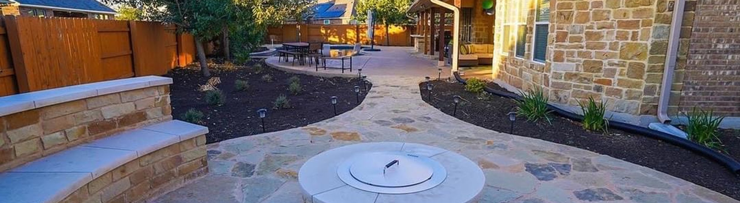 Steiner Ranch, TX backyard with a fire pit, flagstone patio, bench seating wall, and planting beds by Thrive Landscape and Design