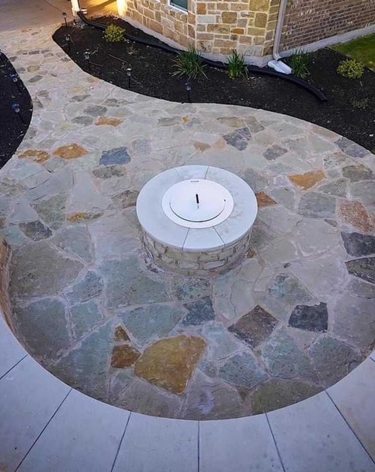 Flagstone fire-pit area with a stone bench seating wall and planting beds at a Steiner Ranch home