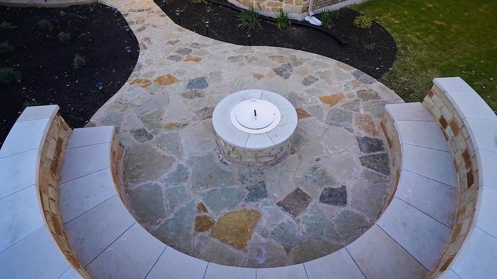 Flagstone fire pit with a stone bench seating wall and planting beds at a Steiner Ranch backyard