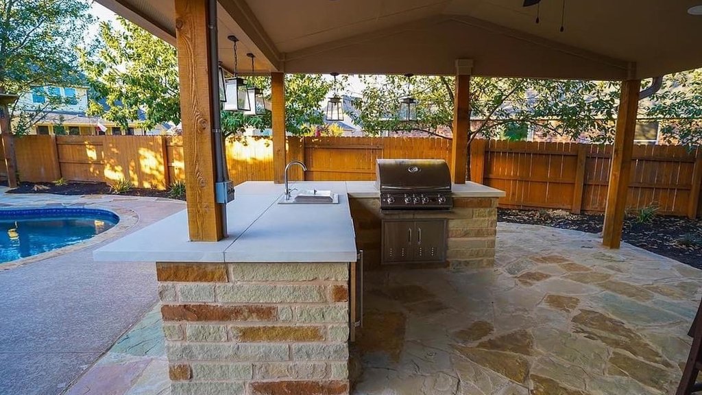 Finished outdoor kitchen with a built-in grill under a pergola beside a pool in Steiner Ranch