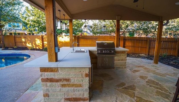 Outdoor kitchen and grill under a pergola beside a pool at a Steiner Ranch home