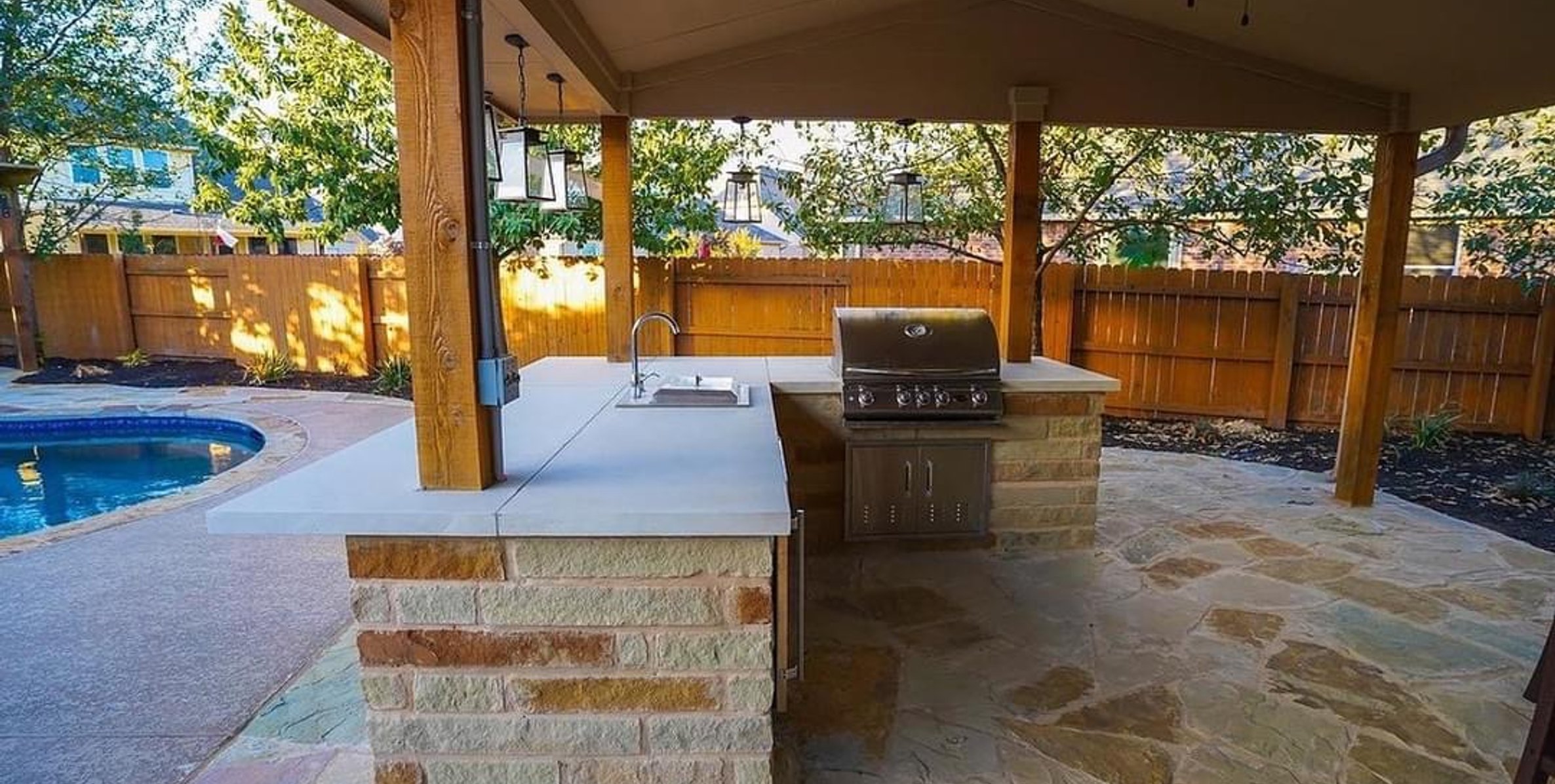 Covered outdoor kitchen with grill and pergola overlooking the flagstone patio and pool