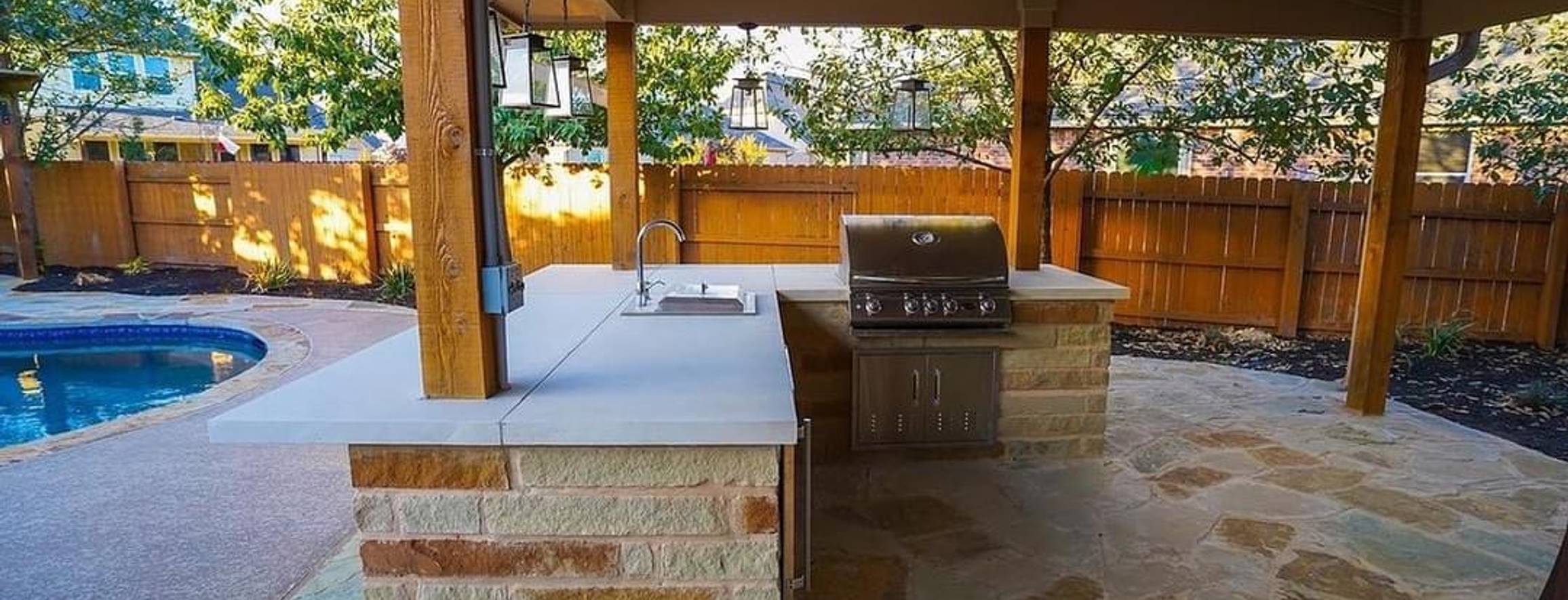 Steiner Ranch backyard with an outdoor kitchen, grill, pergola, flagstone patio, and pool by Thrive Landscape and Design
