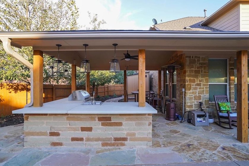 Outdoor kitchen under a pergola beside a pool and flagstone patio in Steiner Ranch