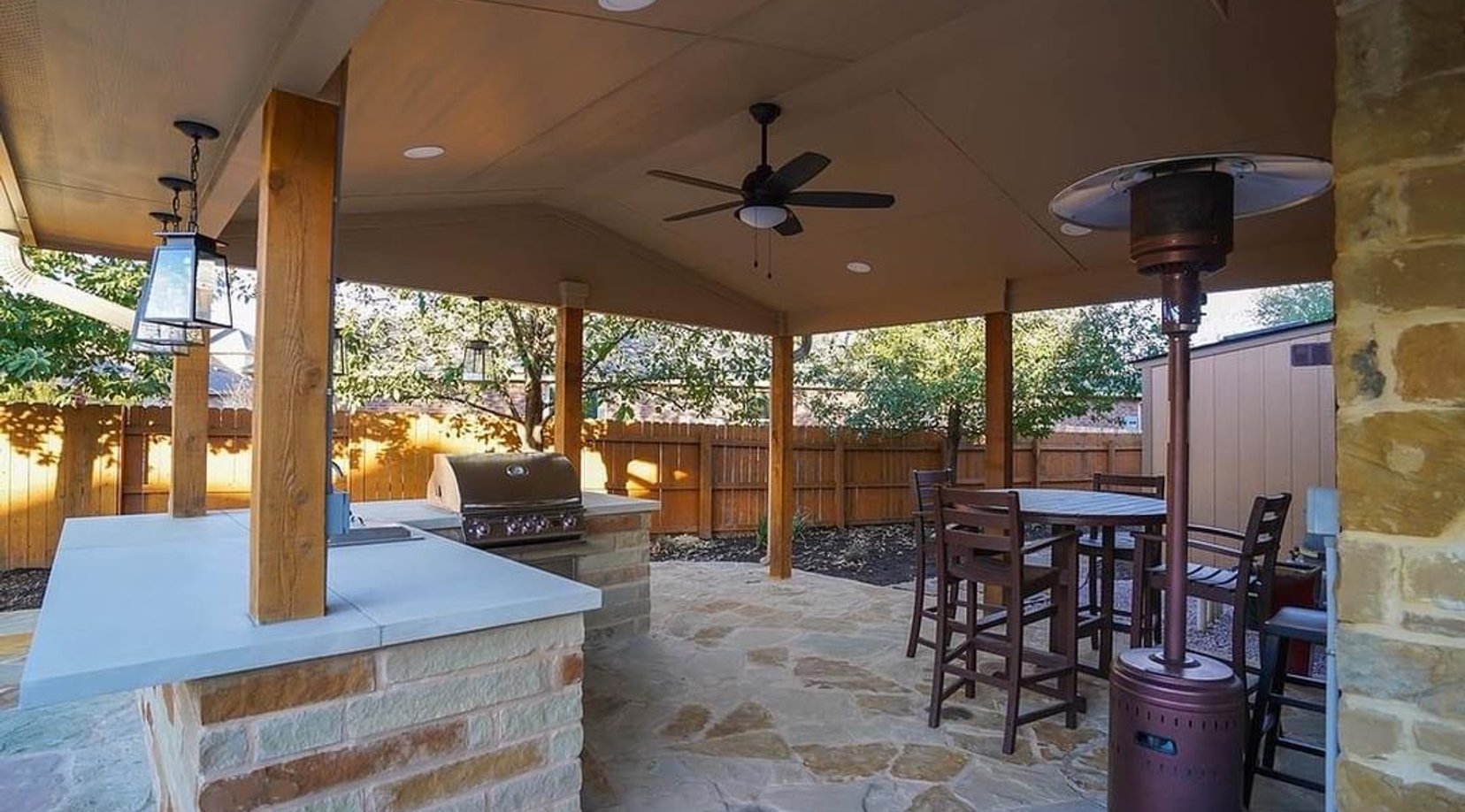 Outdoor kitchen with concrete countertop and stainless steel grill under the pergola